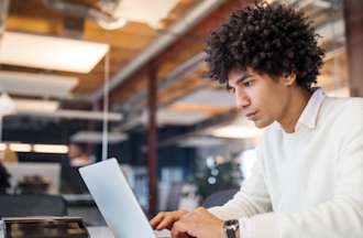 [Featured image] A web designer works on a responsive web design for a client. They are wearing a white sweater and working in an open, industrial office space.