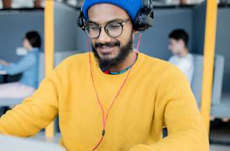 [Featured Image] A man in a yellow sweater types on a laptop in a co-working space.