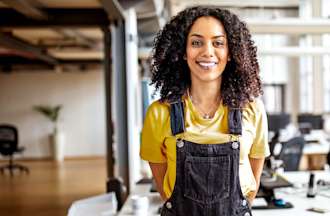 [Featured image] A solutions architect wearing black overalls and a yellow shirt stands alone in an open office.