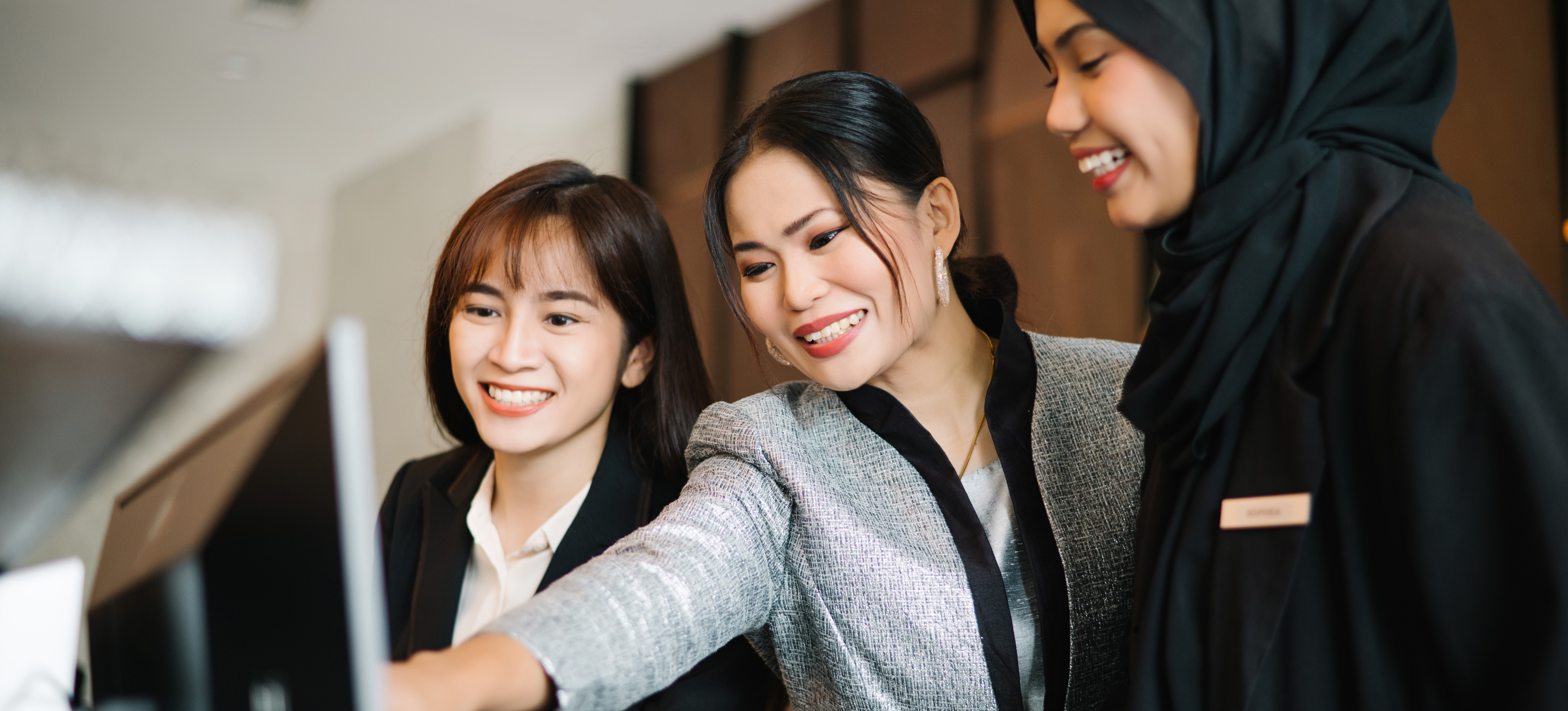 [Featured Image] Three coworkers stand in front of a computer monitor discussing the efficiency of AI productivity tools.
