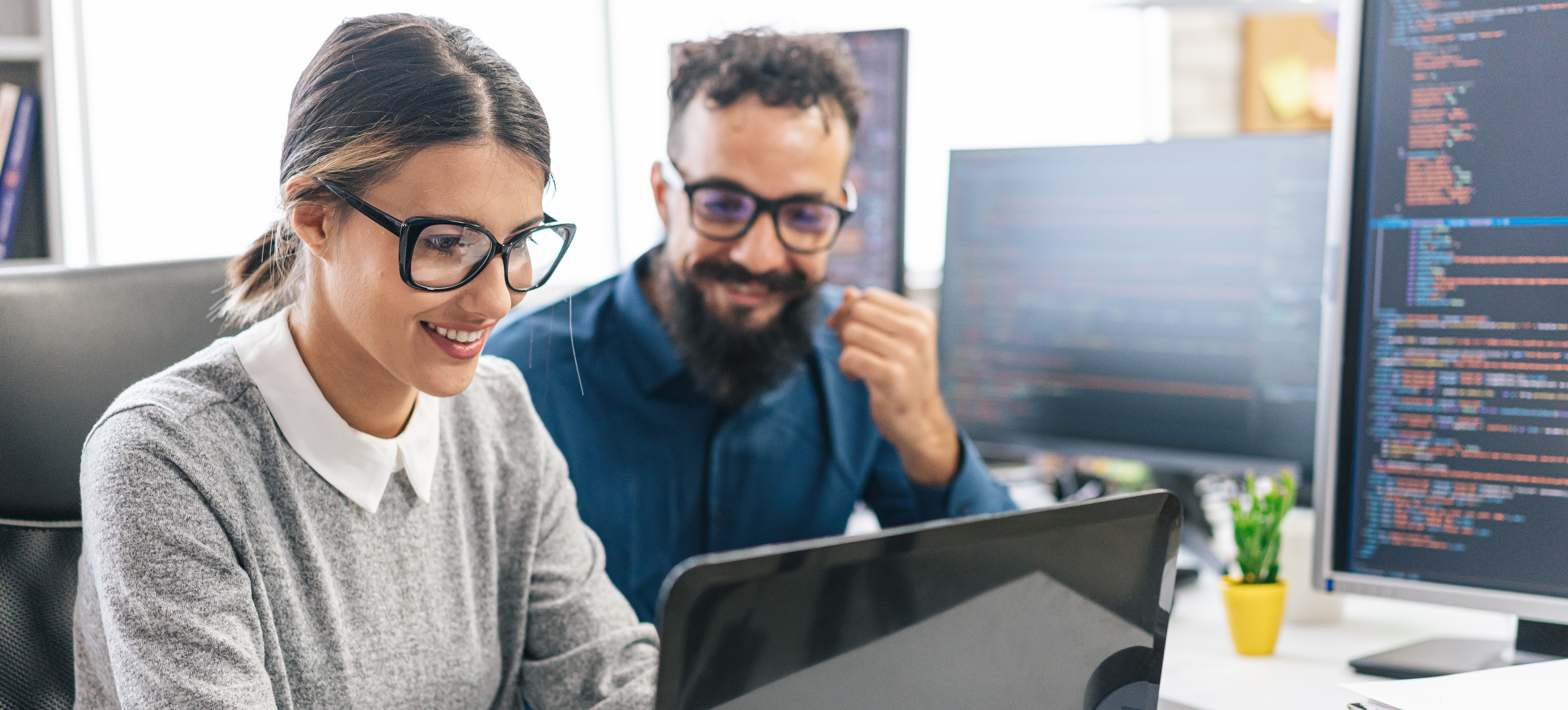 [FEATURED IMAGE] A cybersecurity professional learns a programming language while working on their laptop beside a colleague. 