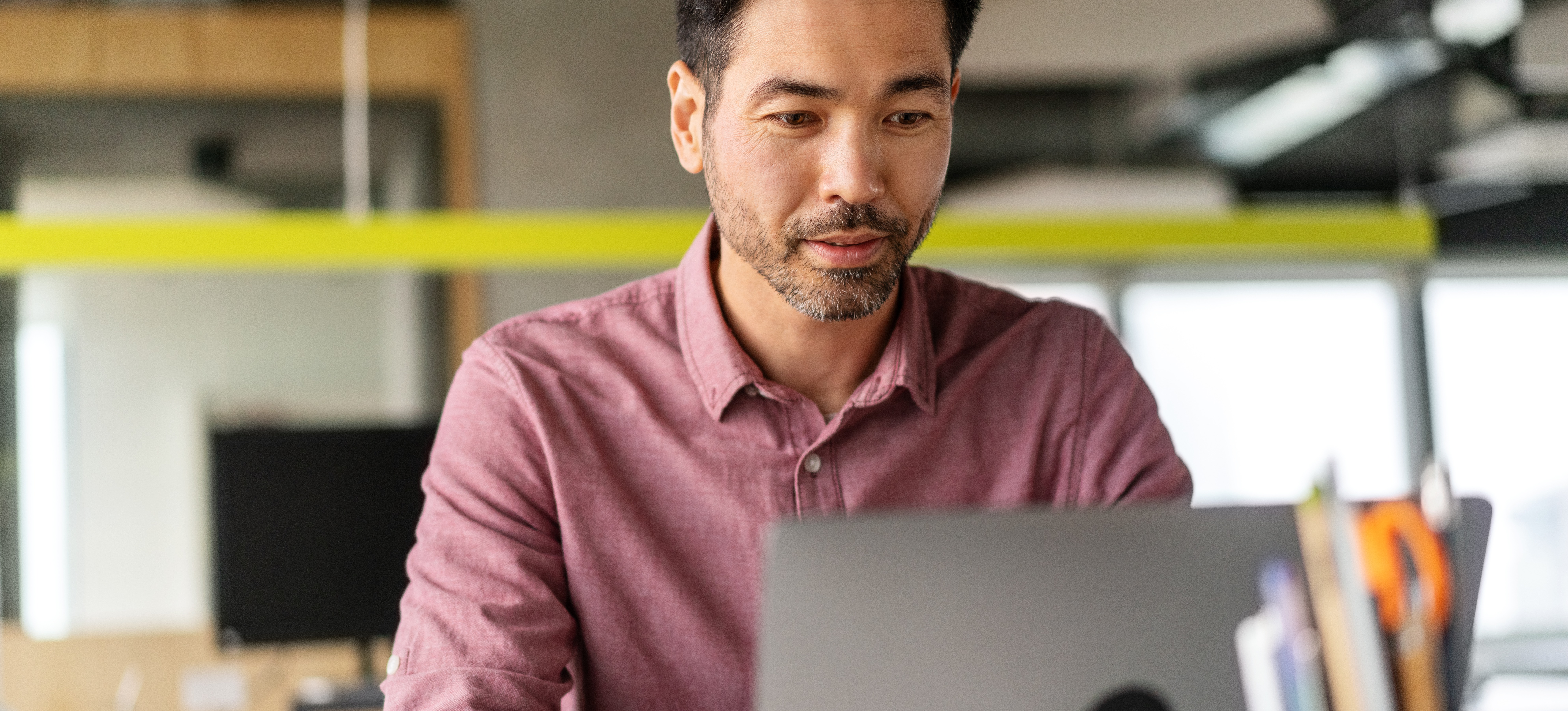 [Hauptbild] Eine Person, die für das Gehalt eines IT-Managers arbeitet, sitzt in einem Büroraum vor ihrem Laptop.