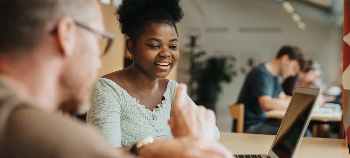 [Featured Image] A learner studies to get their associate degree in computer science, collaborating with a fellow learner as they look at a laptop.
