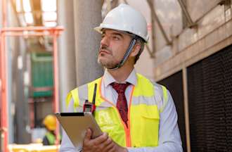 [Featured image] A Man wearing a hard hat inspects a building.
