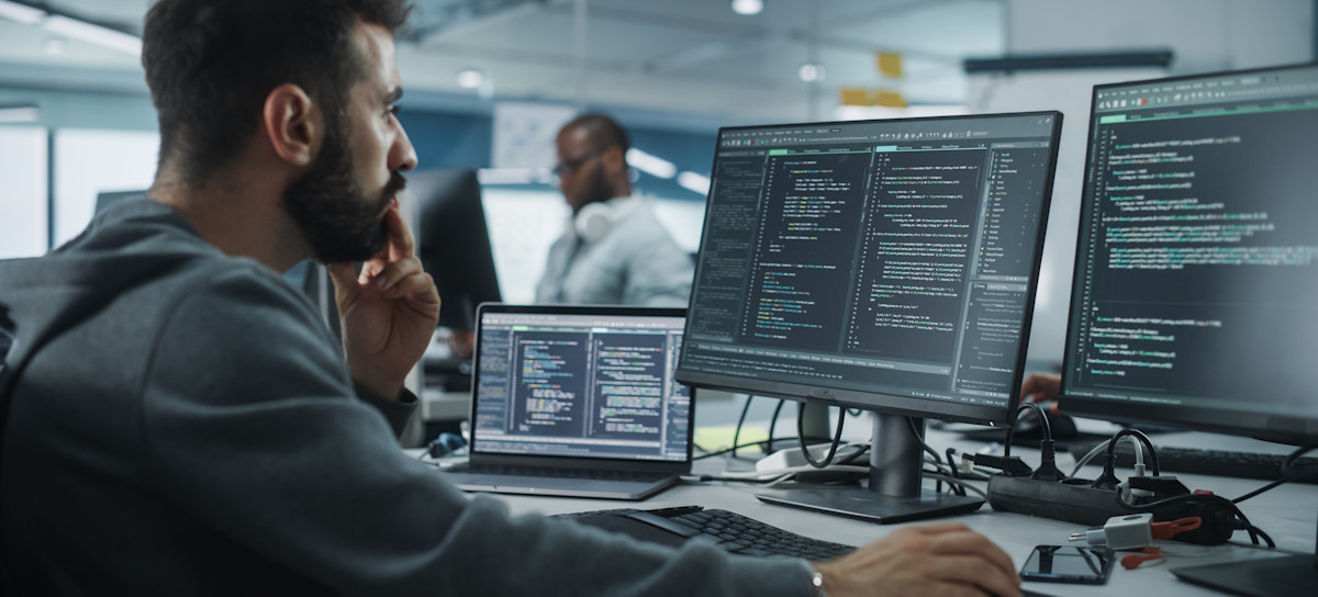[Featured Image] A programmer using go programming language works at their desk, with multiple computers filled with code in front of them.
