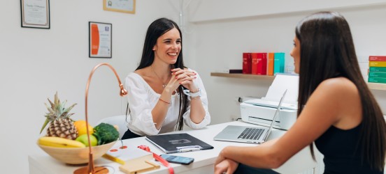 [Featured image] A nutritionist sits at their desk and consults with a client.