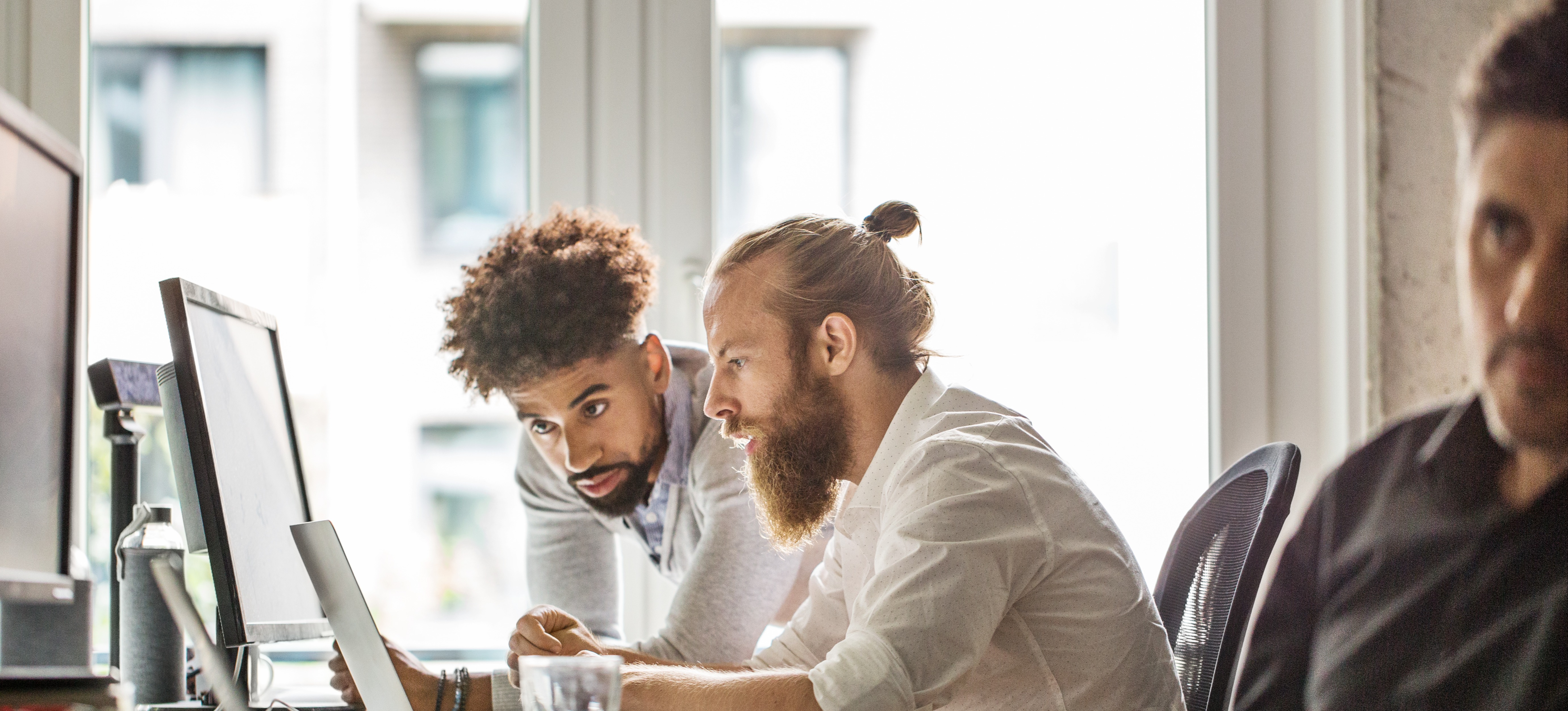 [Featured Image] Two professionals earning a Salesforce developer salary discuss the current project they are collaborating on. 
