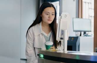 [Featured Image] A woman holding coffee and monitoring cybersecurity in health care environment.
