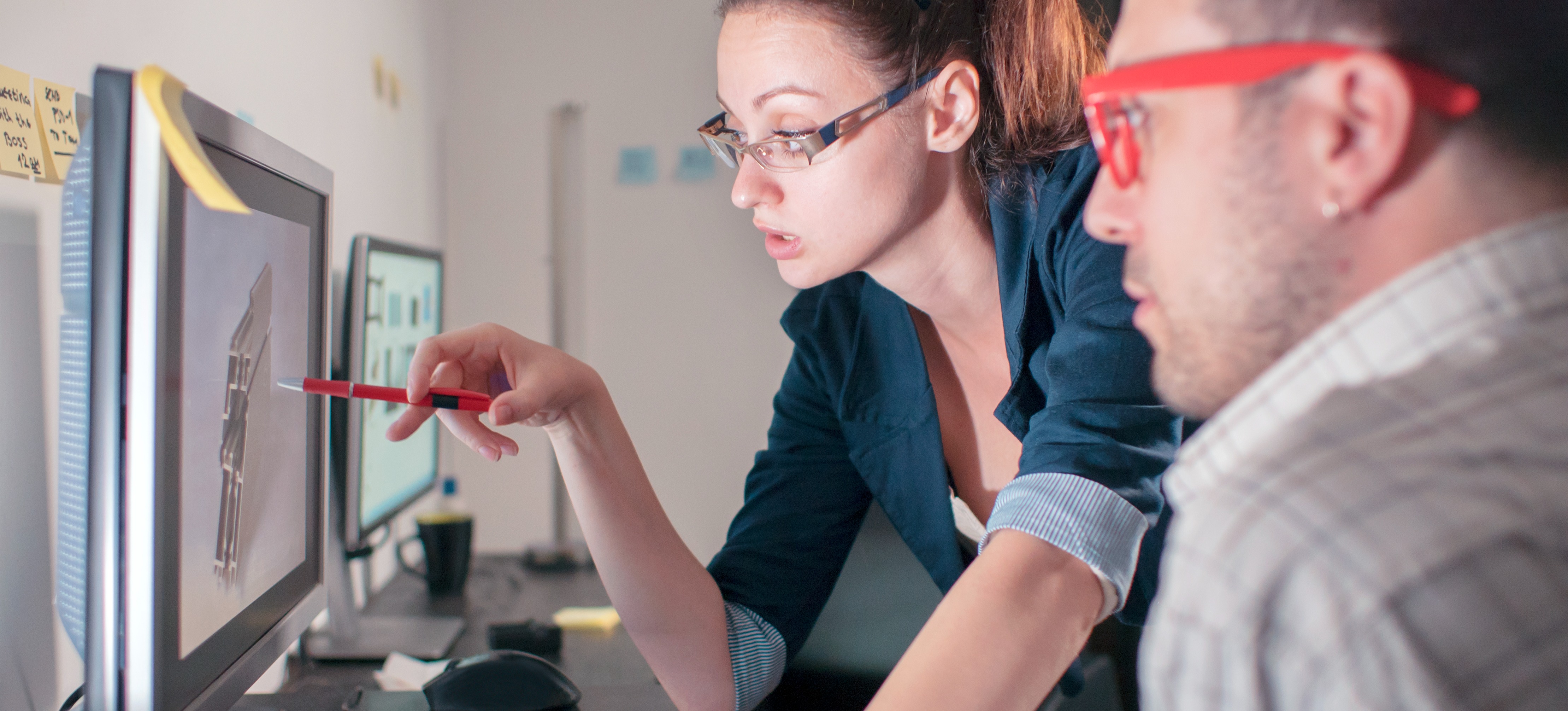 [Featured Image] Colleagues in a professional workspace interact in front of a computer and discuss the core competencies of computer vision skills.
