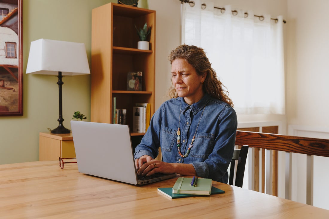 [Featured image] A Woman wearing a blue buttoned top sits at her dining table and browses online for how to set up Google Analytics for her website.