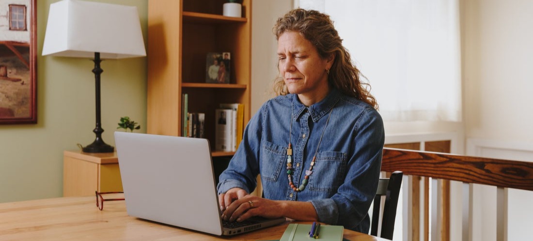 [Featured image] A Woman wearing a blue buttoned top sits at her dining table and browses online for how to set up Google Analytics for her website.