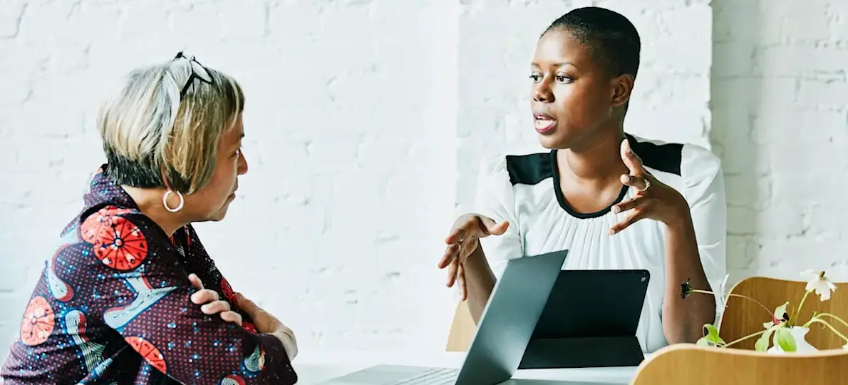 [Featured image] A business analyst interviews an employee. Both of them have their laptops in front of them.