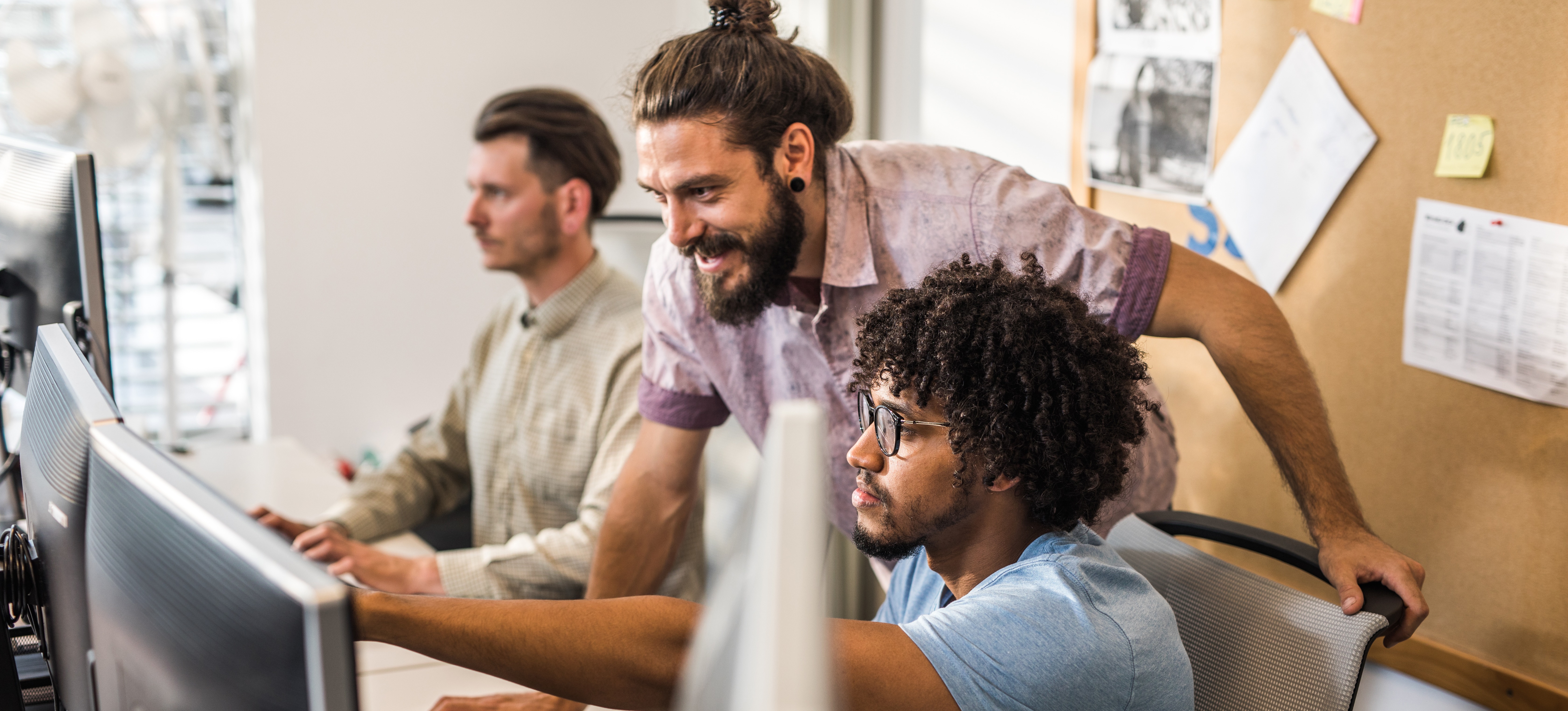 [Featured Image] An application developer is at a computer showing his project to a co-worker.