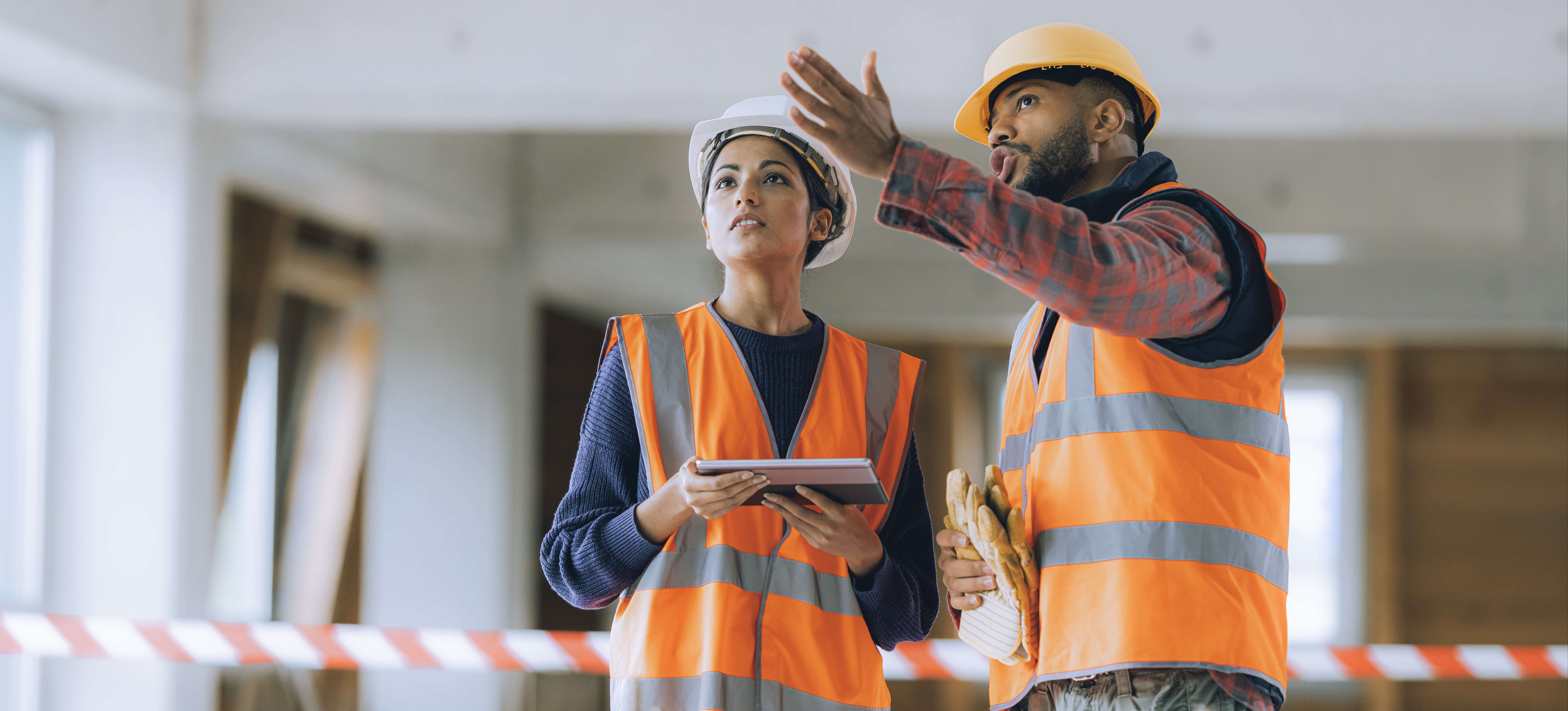 [Featured Image] Wearing a hard hat and orange vest, a construction manager, one of the highest paying construction jobs, talks to his colleague on a construction site.
