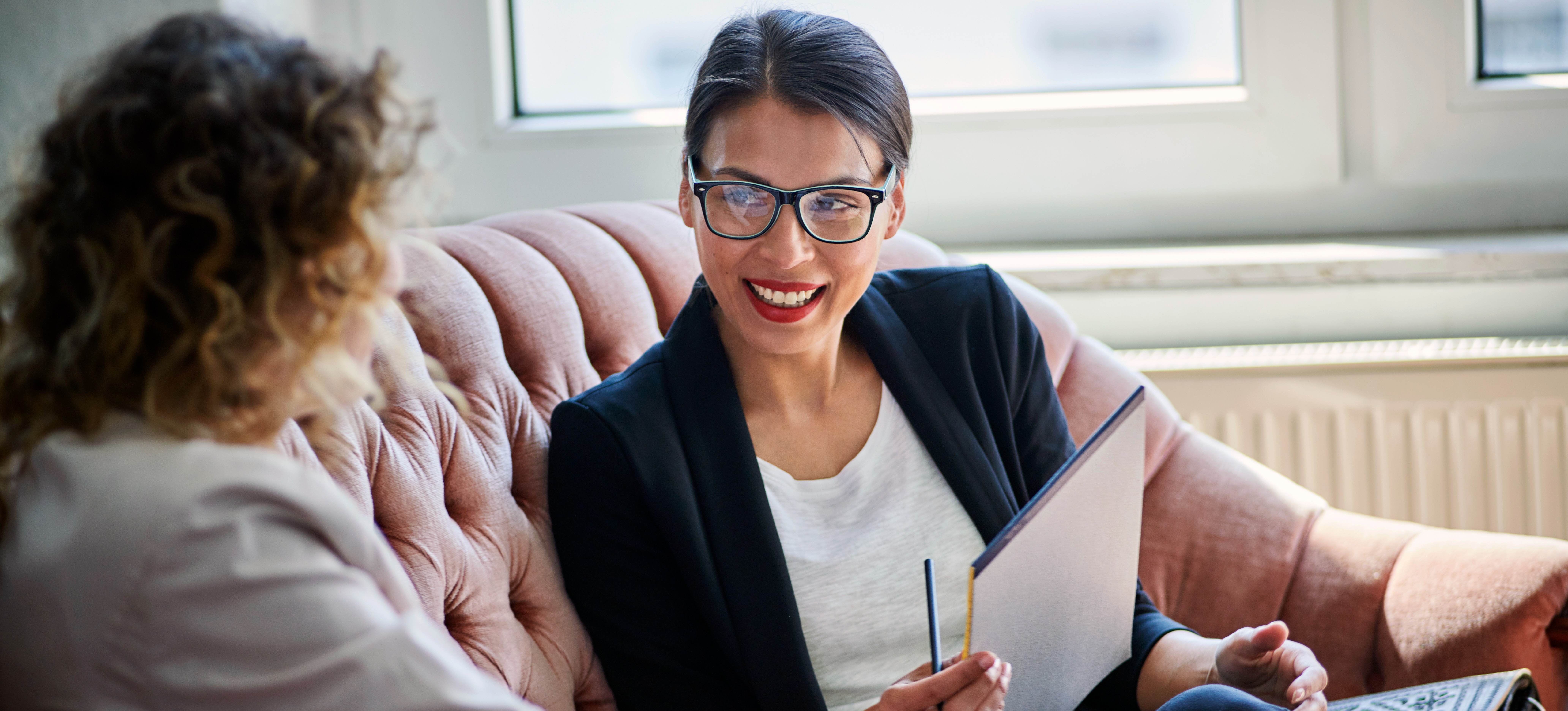 [Featured Image] Person in glasses interviewing a second person using STAR interview questions while sitting on a couch in an office