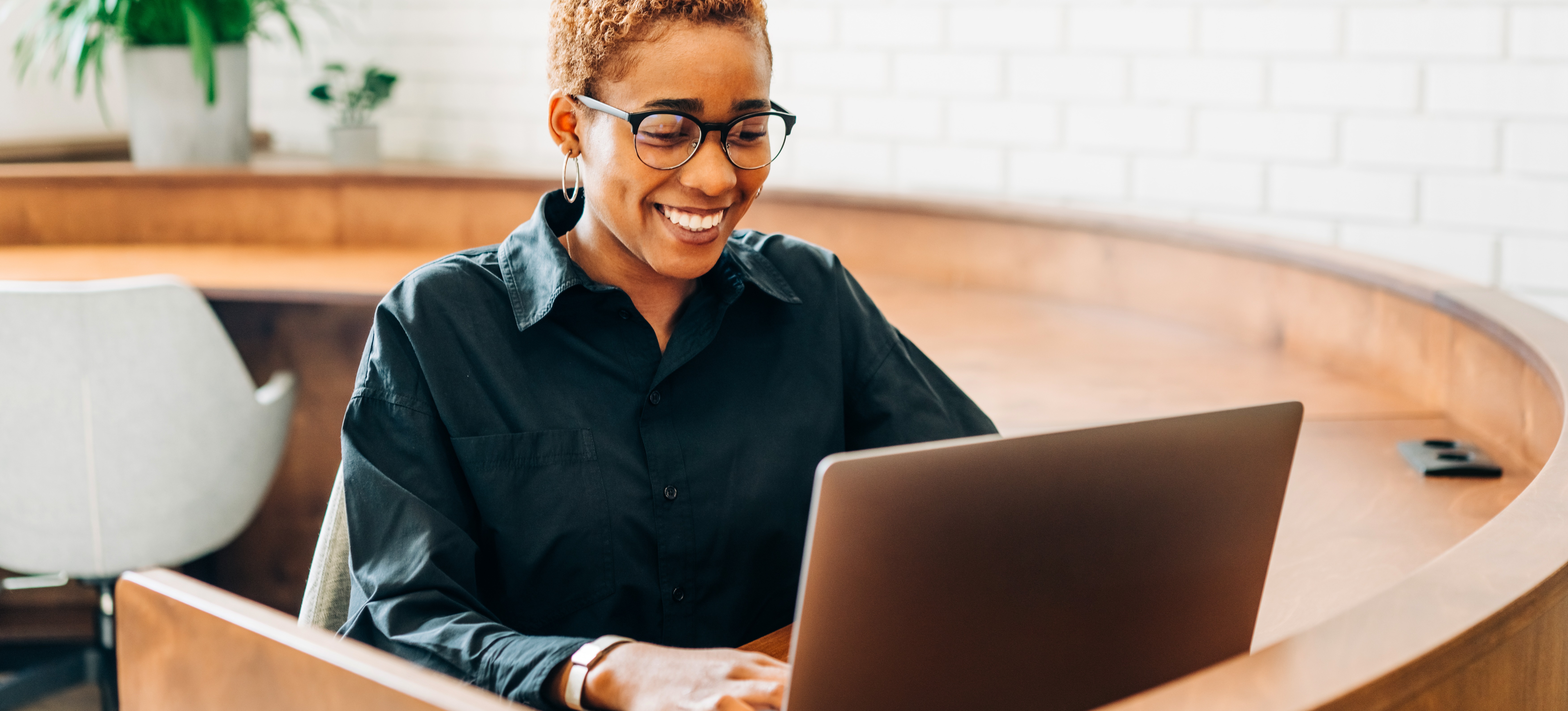 [Featured Image]: A woman works on a laptop and smiles after learning how to write a cover letter when applying for jobs.