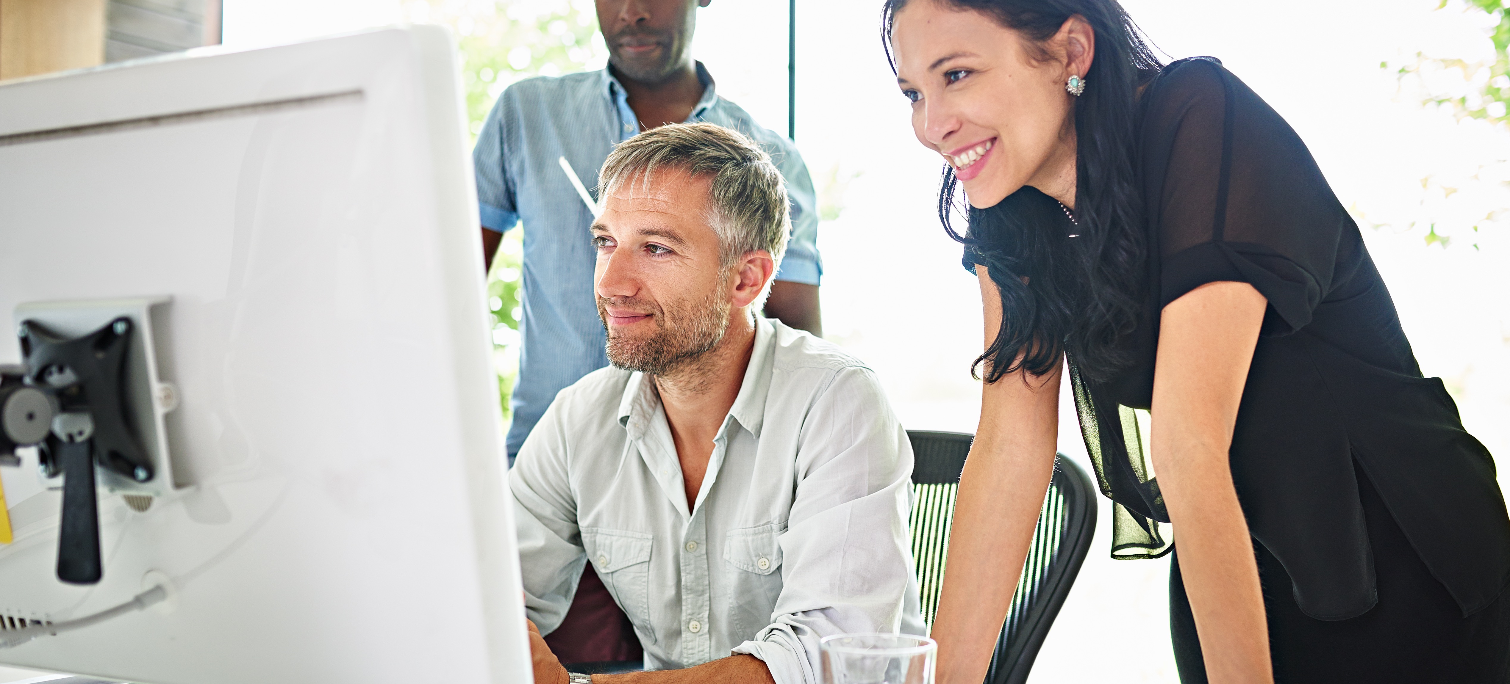 [Featured Image]: Three computer science colleagues stand in an office looking at a computer.