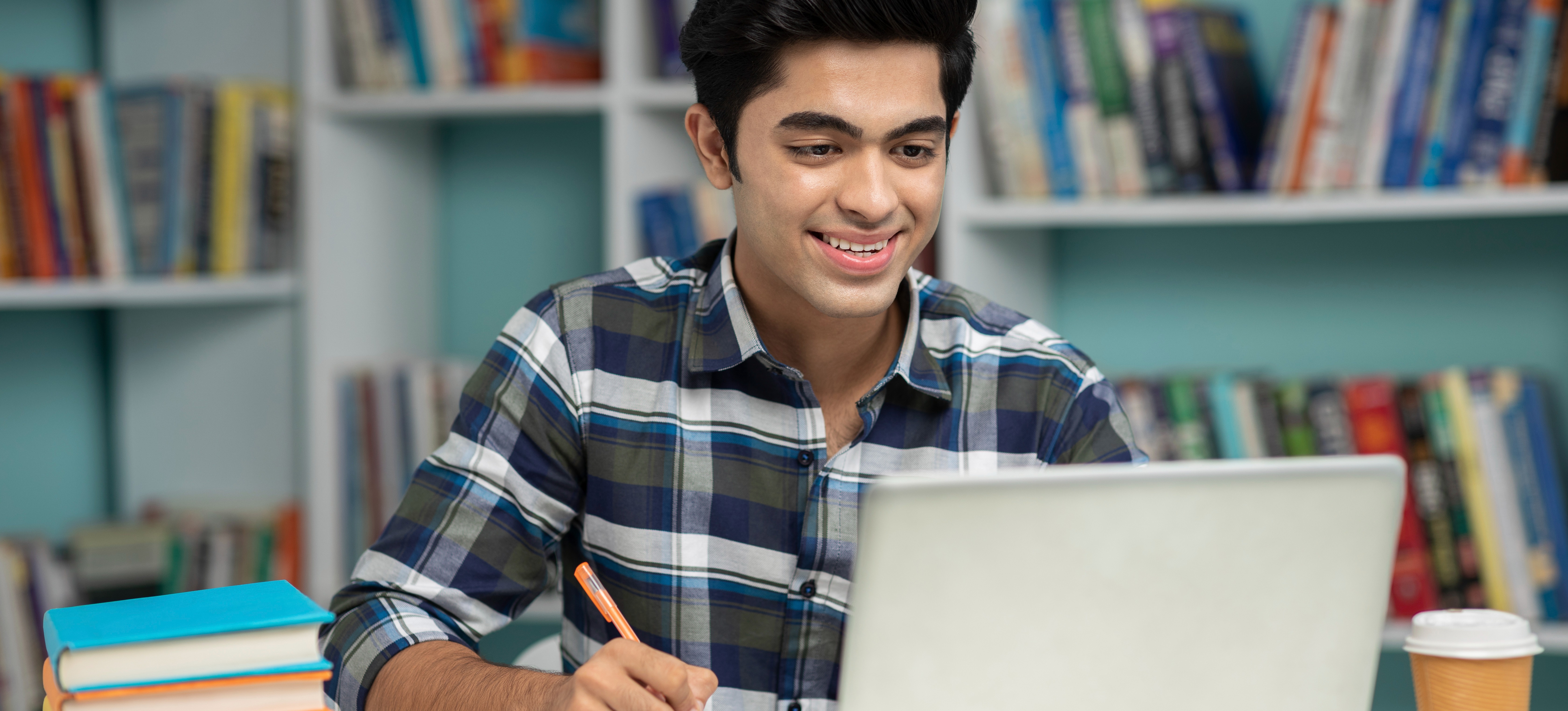 [Featured image] A young student wearing a white sweater uses their laptop in an office setting. 