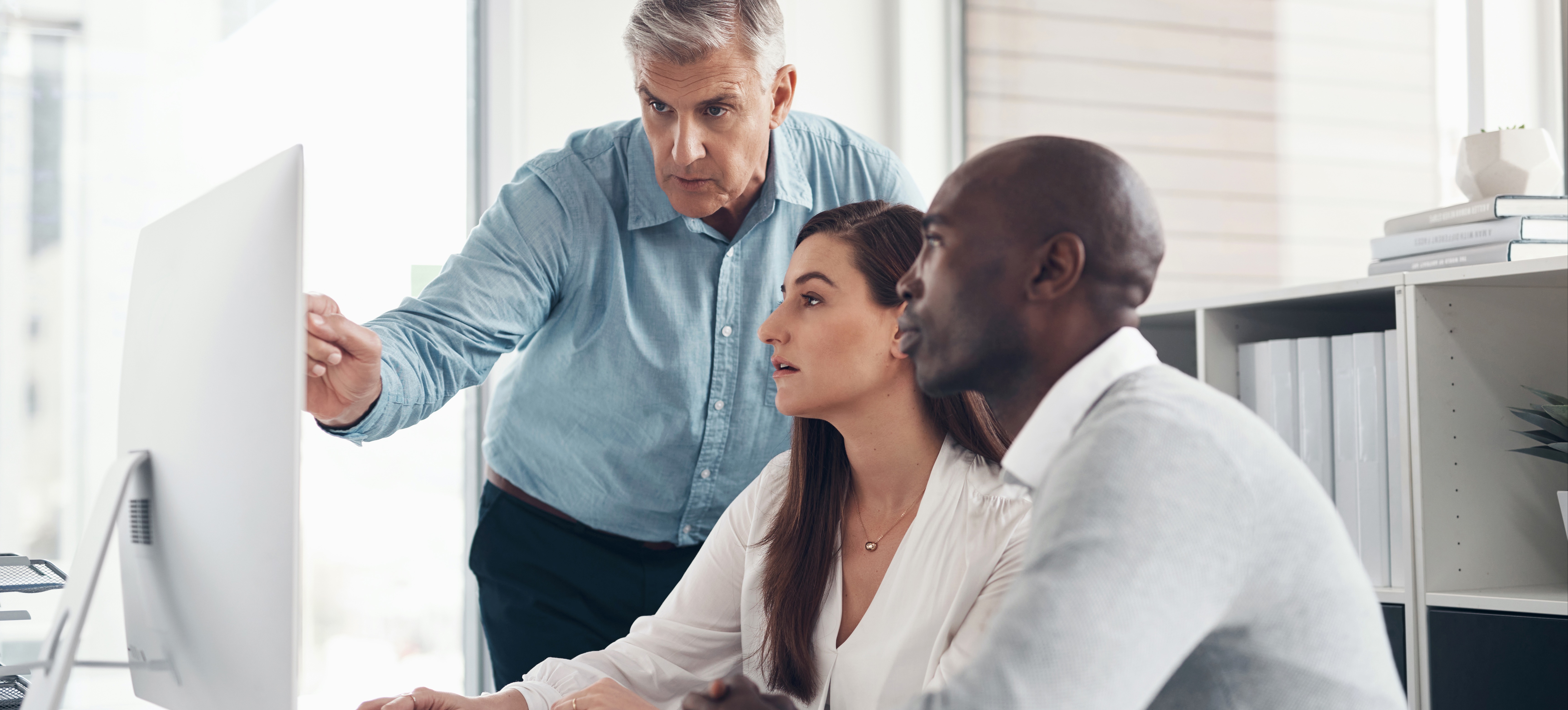 [Feature Image] Two IoT security professionals review IoT security certification options with their mentor as they each decide on the pathways that make sense for their backgrounds and goals.