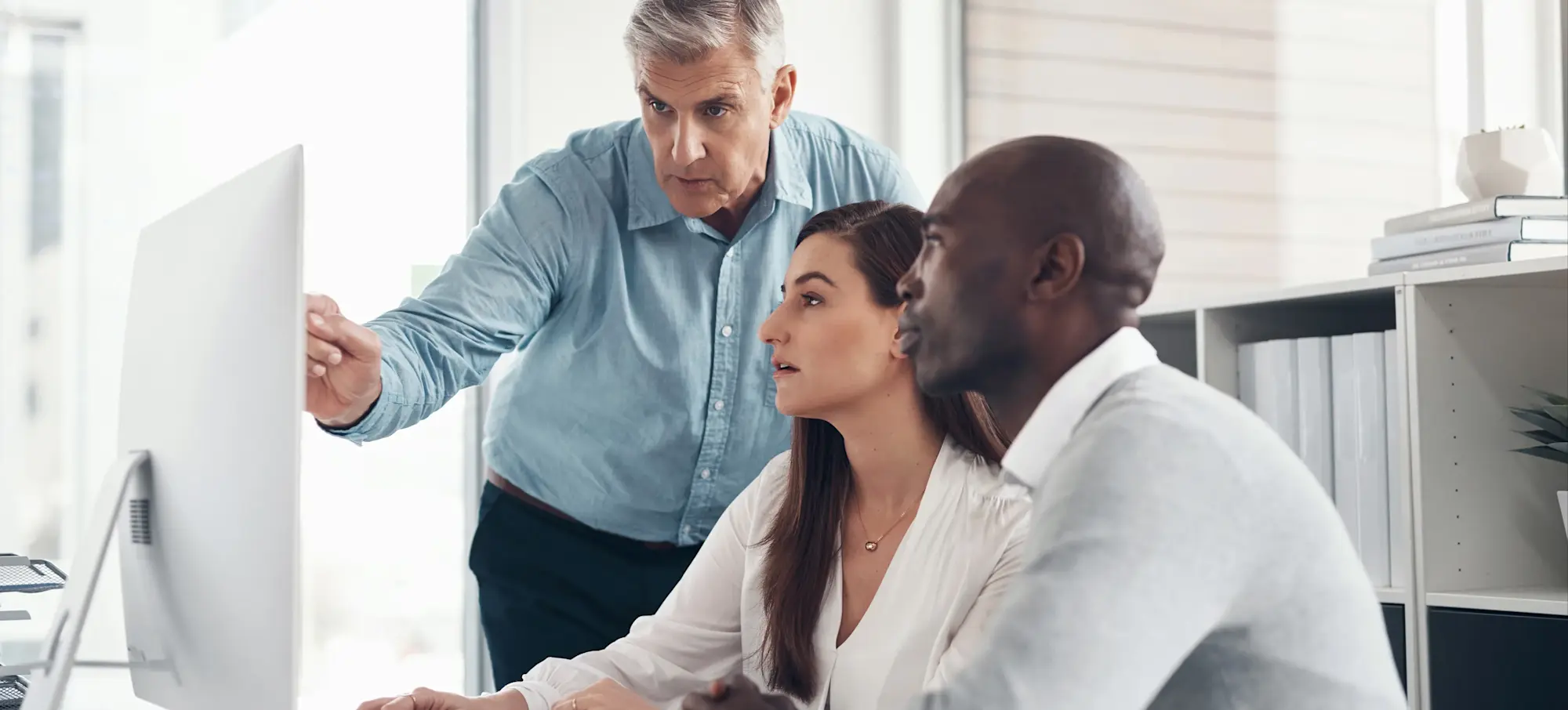[Feature Image] Two IoT security professionals review IoT security certification options with their mentor as they each decide on the pathways that make sense for their backgrounds and goals.