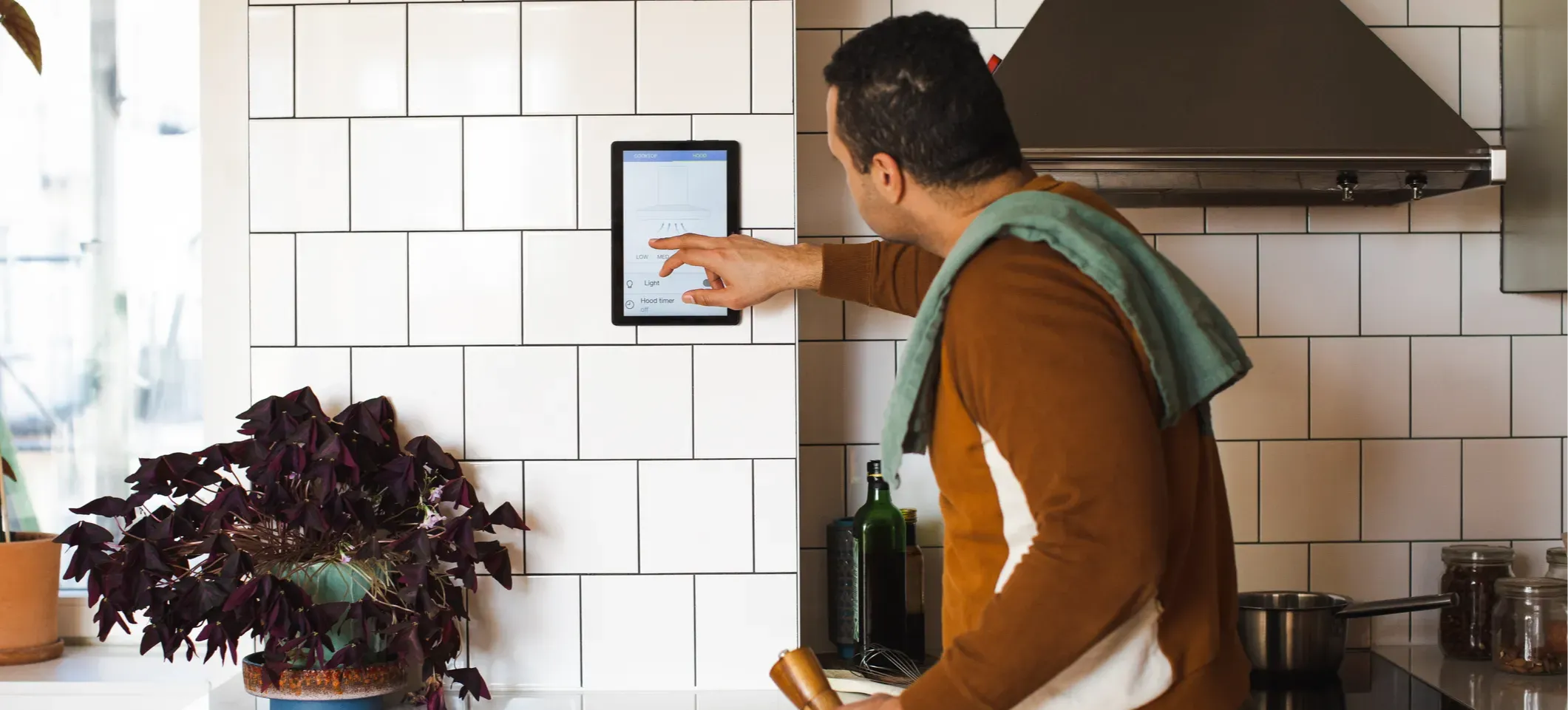 [Featured Image]: A person stands in a kitchen touching a smart home device that's part of the Internet of Things.
