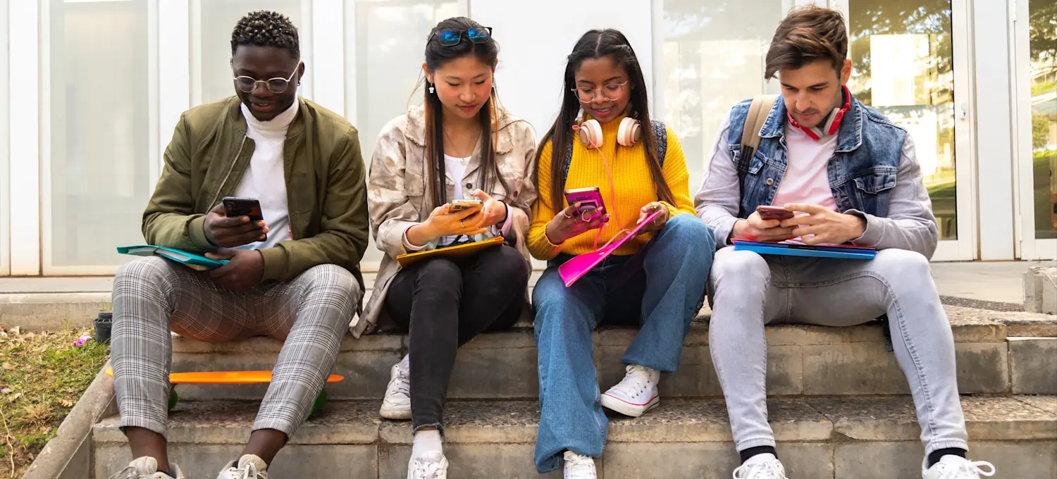 A group of four students pursuing their associate degrees sit on the steps of their school. 