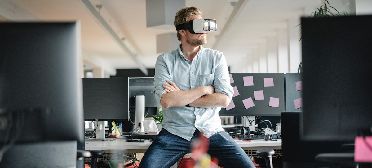 [Featured Image] A VR worker tests virtual realty goggles at their desk.