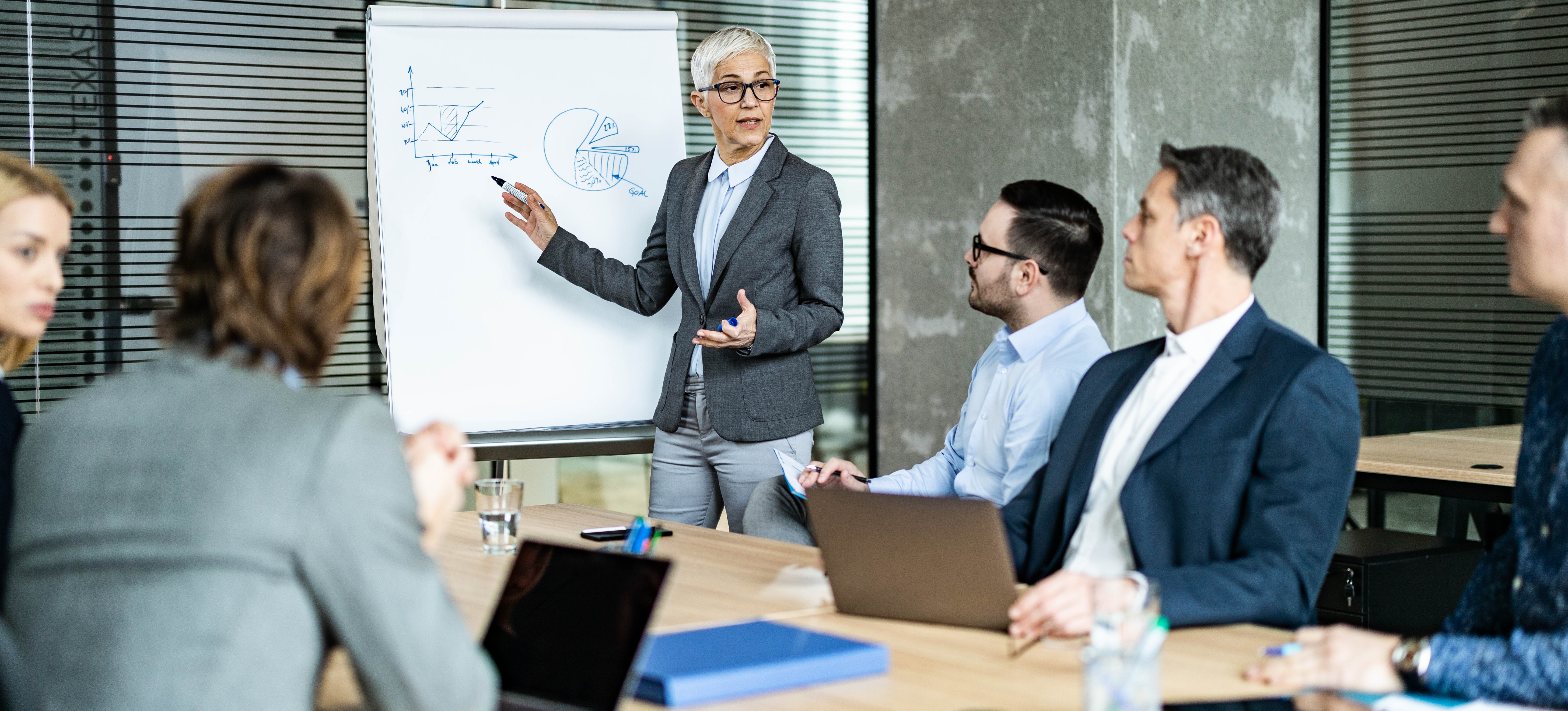 [Featured Image] A business leader presenting salary trends and certification benefits to executives in a professional setting, highlighting insights on PMP certification.
