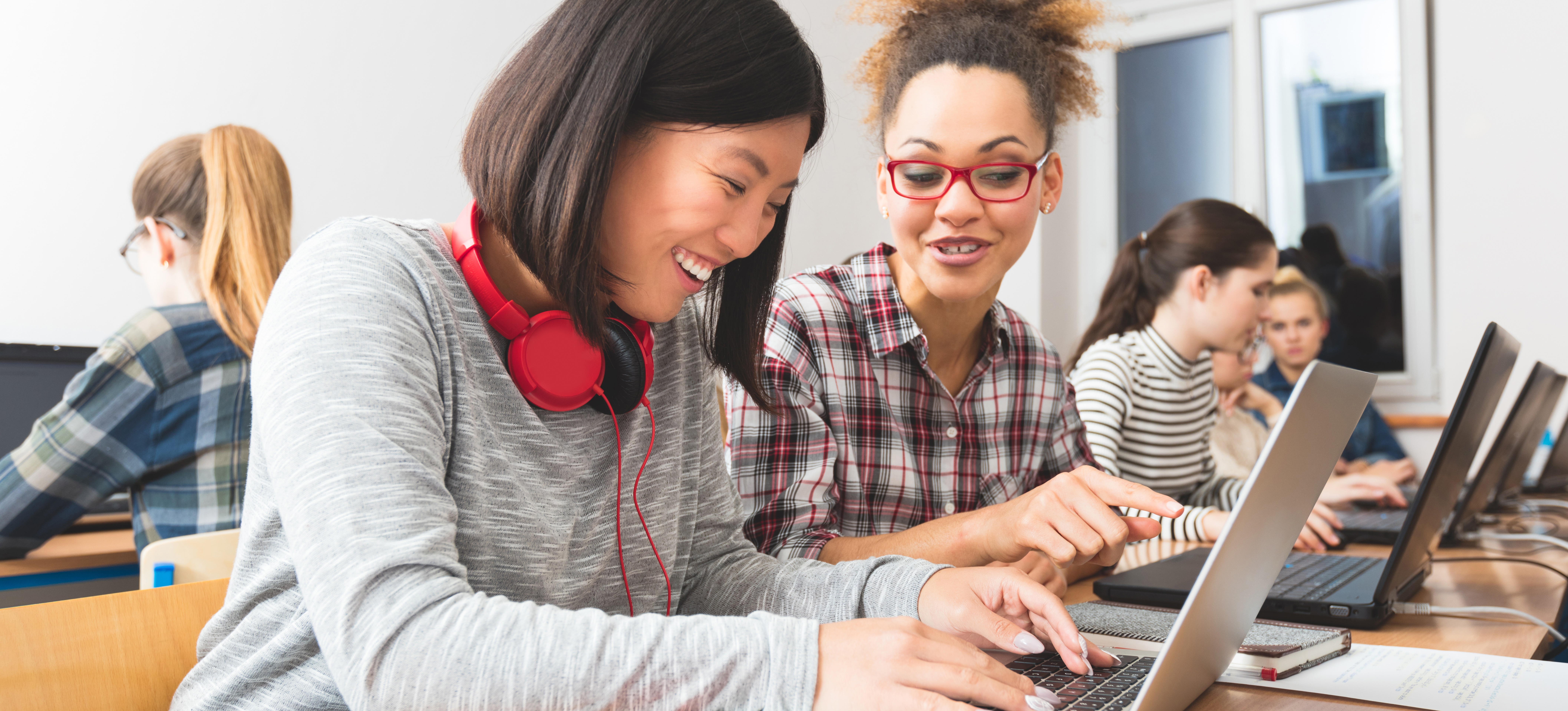[Featured Image] Two women work side by side on laptop computers.