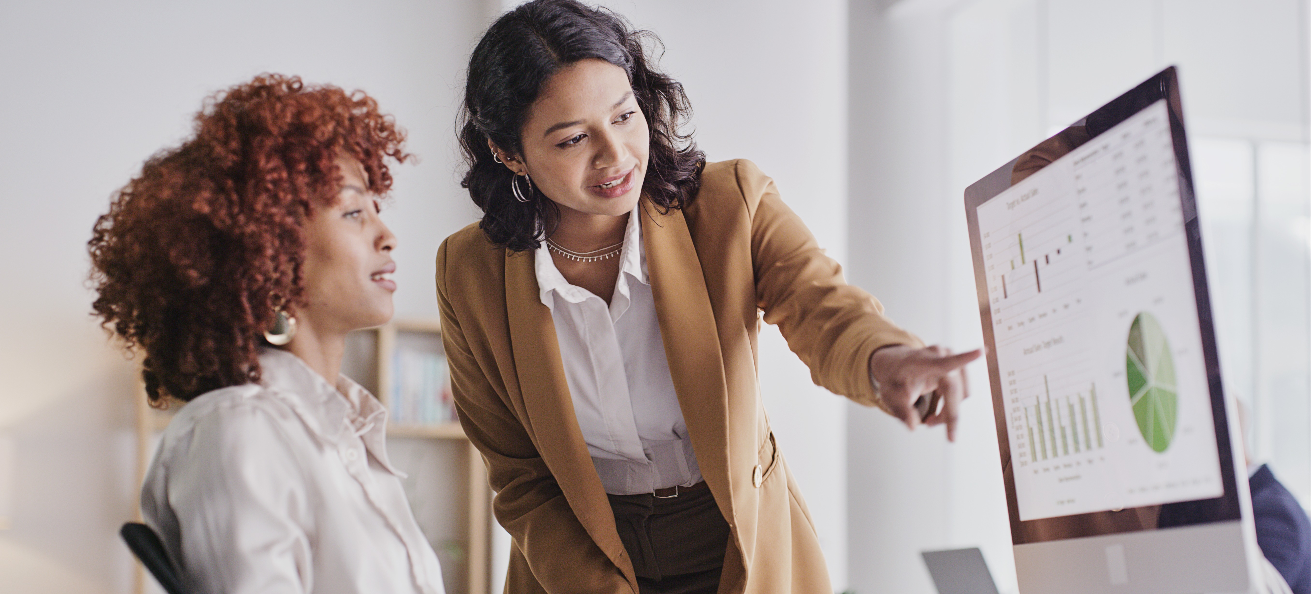 [Featured Image] A data management specialist points to graphs and charts on their colleague's computer screen.
