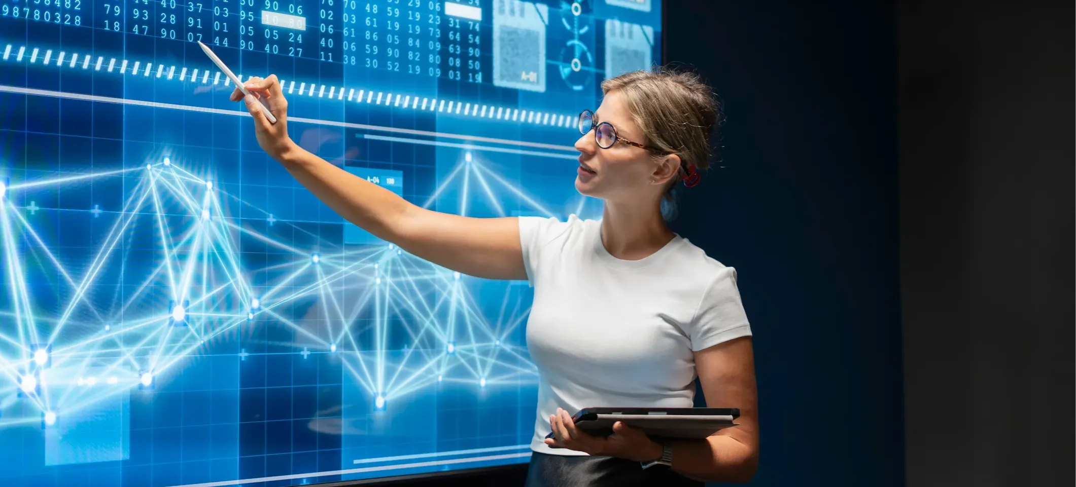 [Featured image] A data scientist points to a large monitor displaying charts that visually represent data.

