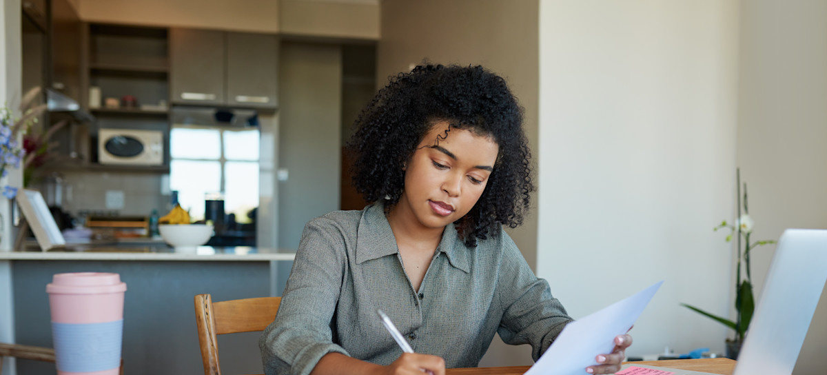 [Featured Image] A job applicant sits at their home desk with a pen in hand and works on their combination resume.