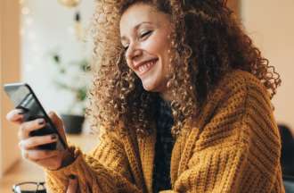 [Featured image] A person with curly hair wearing a yellow sweater searches the internet on a smartphone from a cafe.