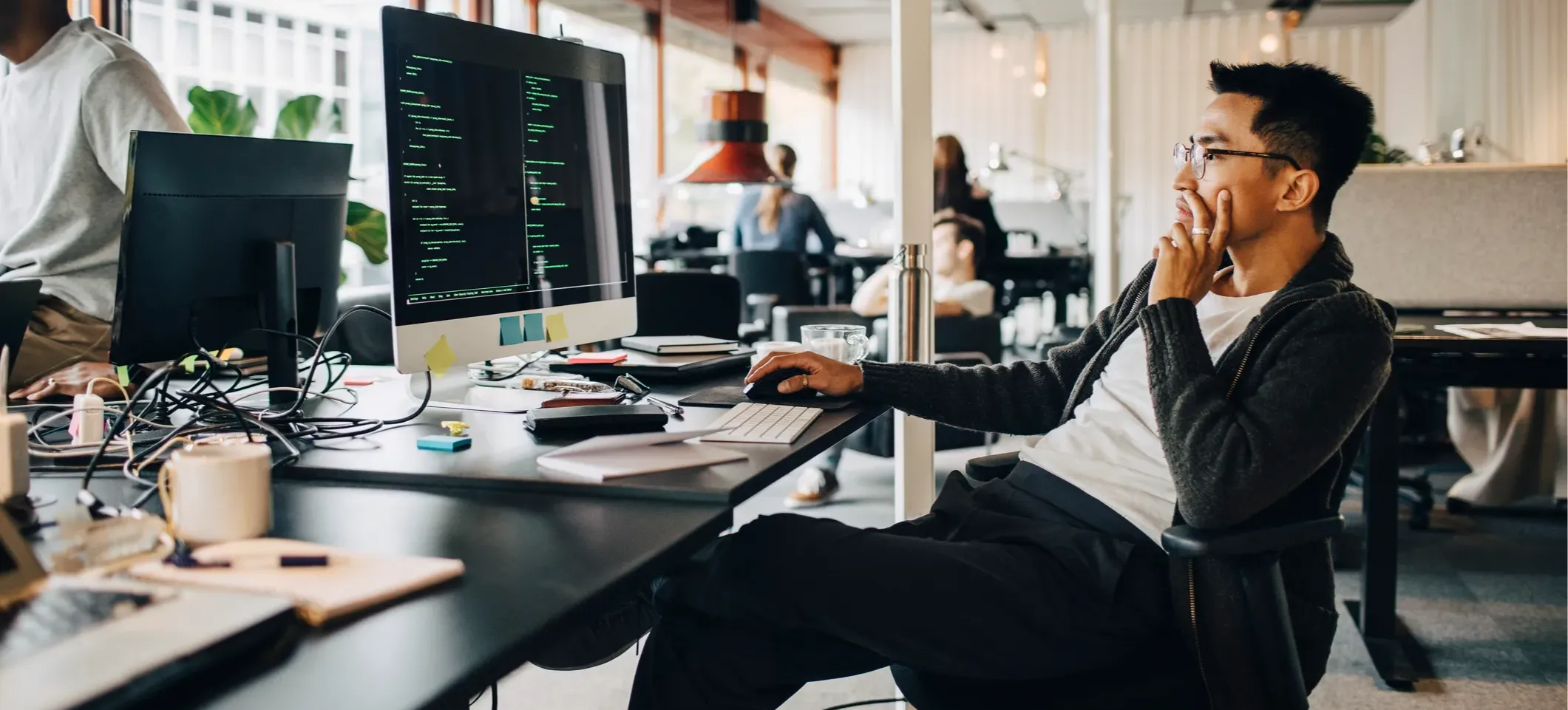[Featured Image] A programmer uses AI coding as they sit in front of a computer screen in an open office.
