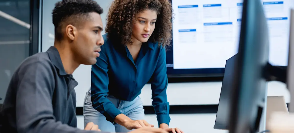 [Featured Image] Two security analysts who earn a competitive CompTIA Security+ salary look at a computer screen in an office.