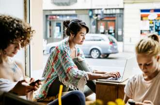 [Featured image] Woman sitting at a café searching for extracurricular activities on her laptop.