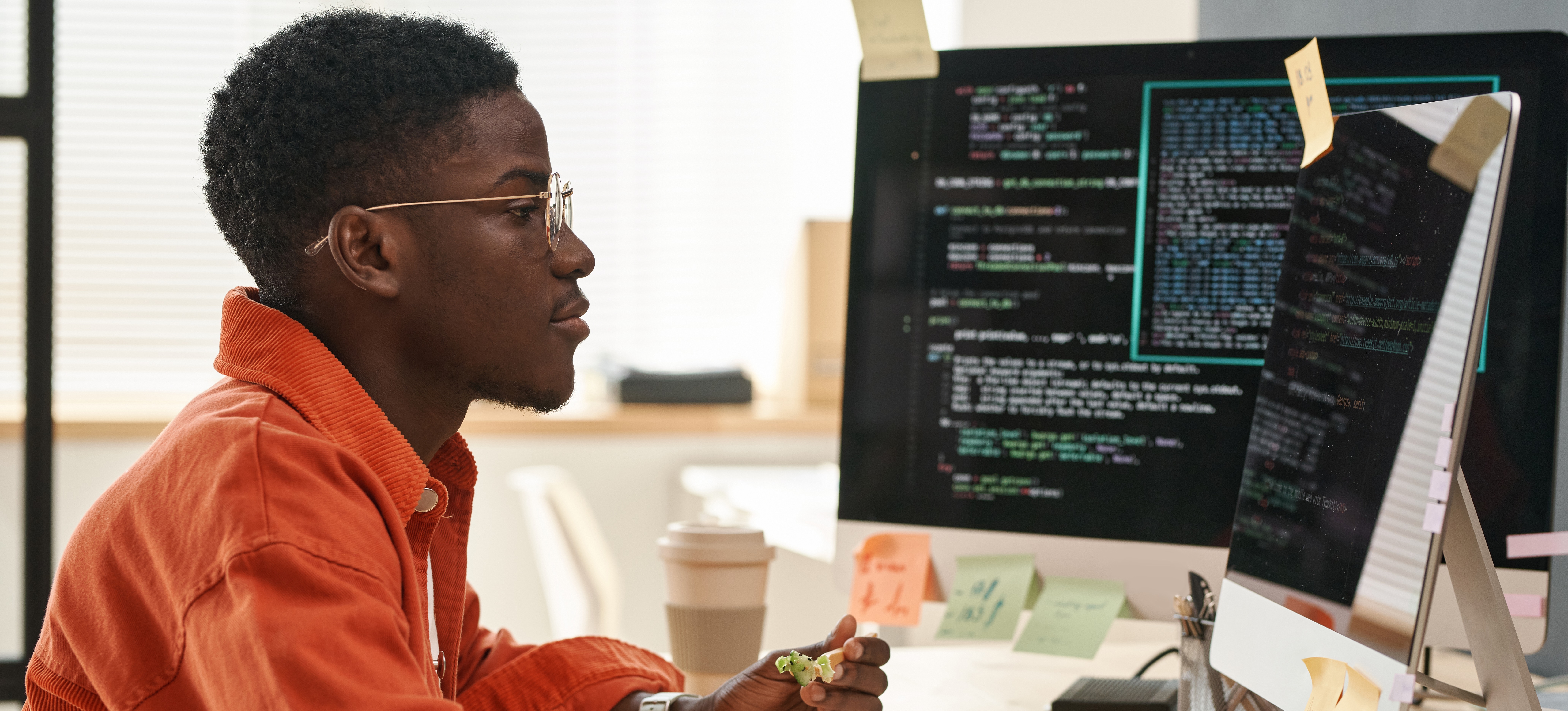 [Featured Image] A person wearing an orange buttondown shirt and glasses earns a data engineer salary as they work at a computer in a sunny home office.
