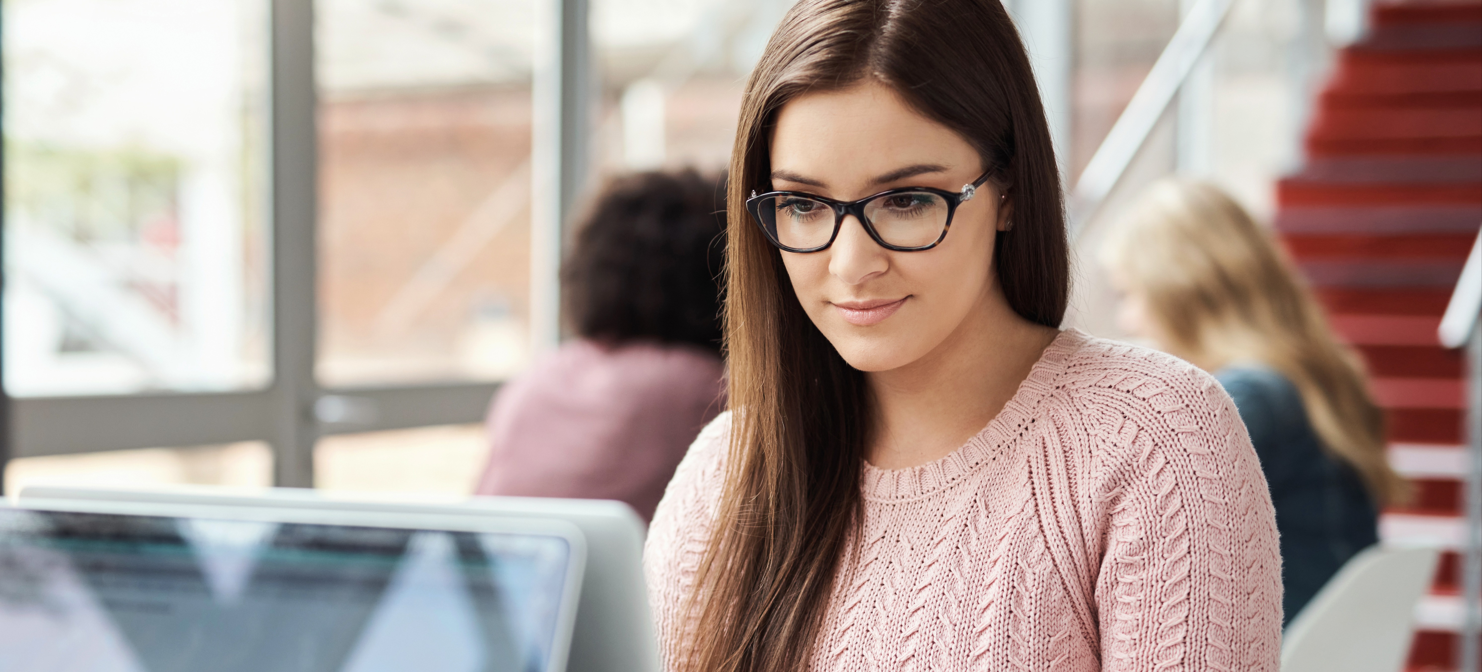 [Featured Image] A student wearing glasses uses a laptop to research the various degree levels in the UK. 