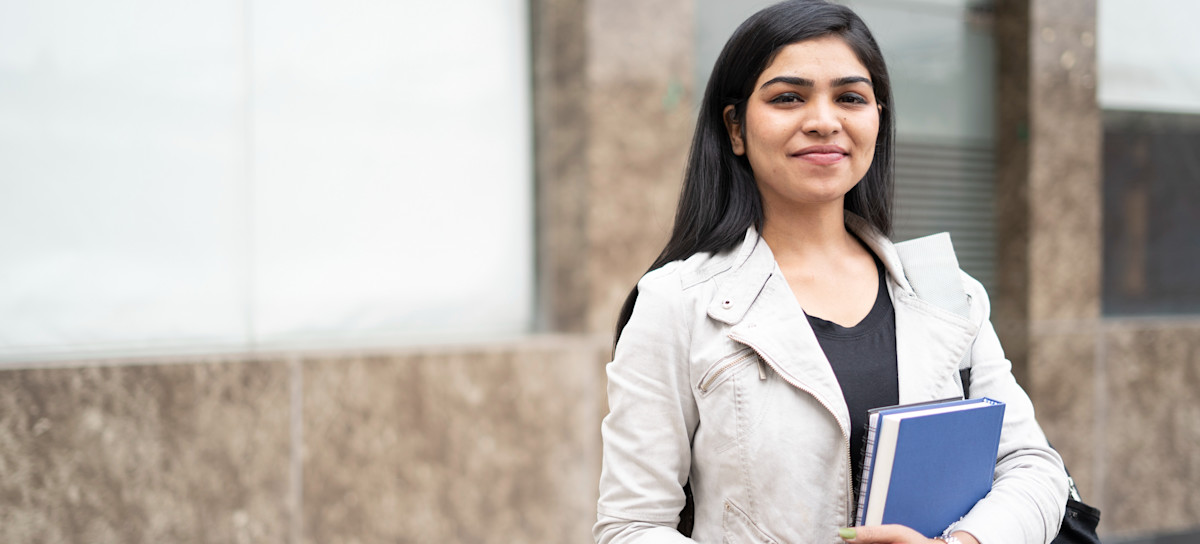 [Featured Image] A student stands outside holding textbooks.