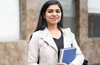 [Featured Image] A female student stands outside holding textbooks.