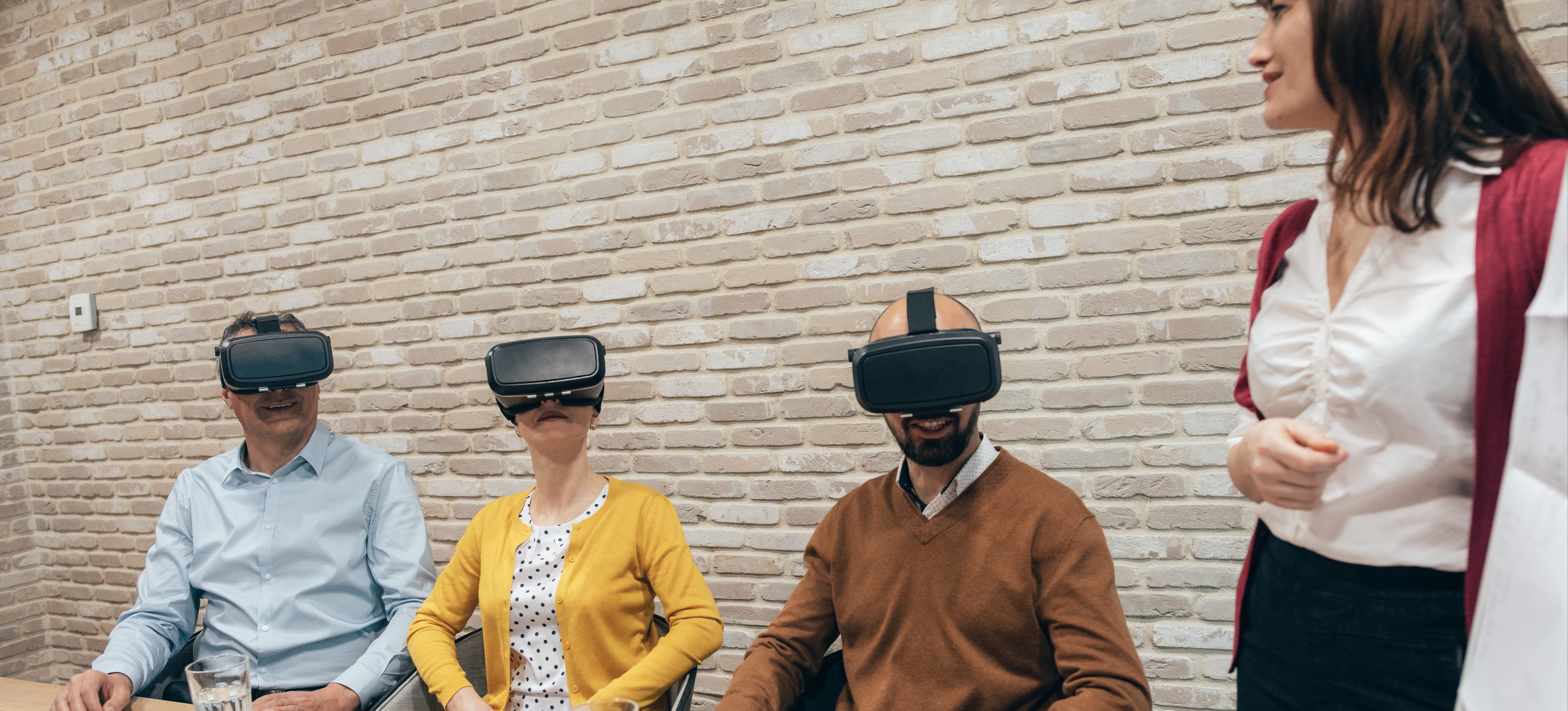 [Featured Image] A group of colleagues sit in a business meeting wearing virtual reality headsets and experimenting with VR, one of the top business intelligence trends. 
