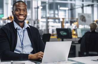 [Featured Image] A back-end developer in a blue shirt and blazer works on a laptop in an open office space.