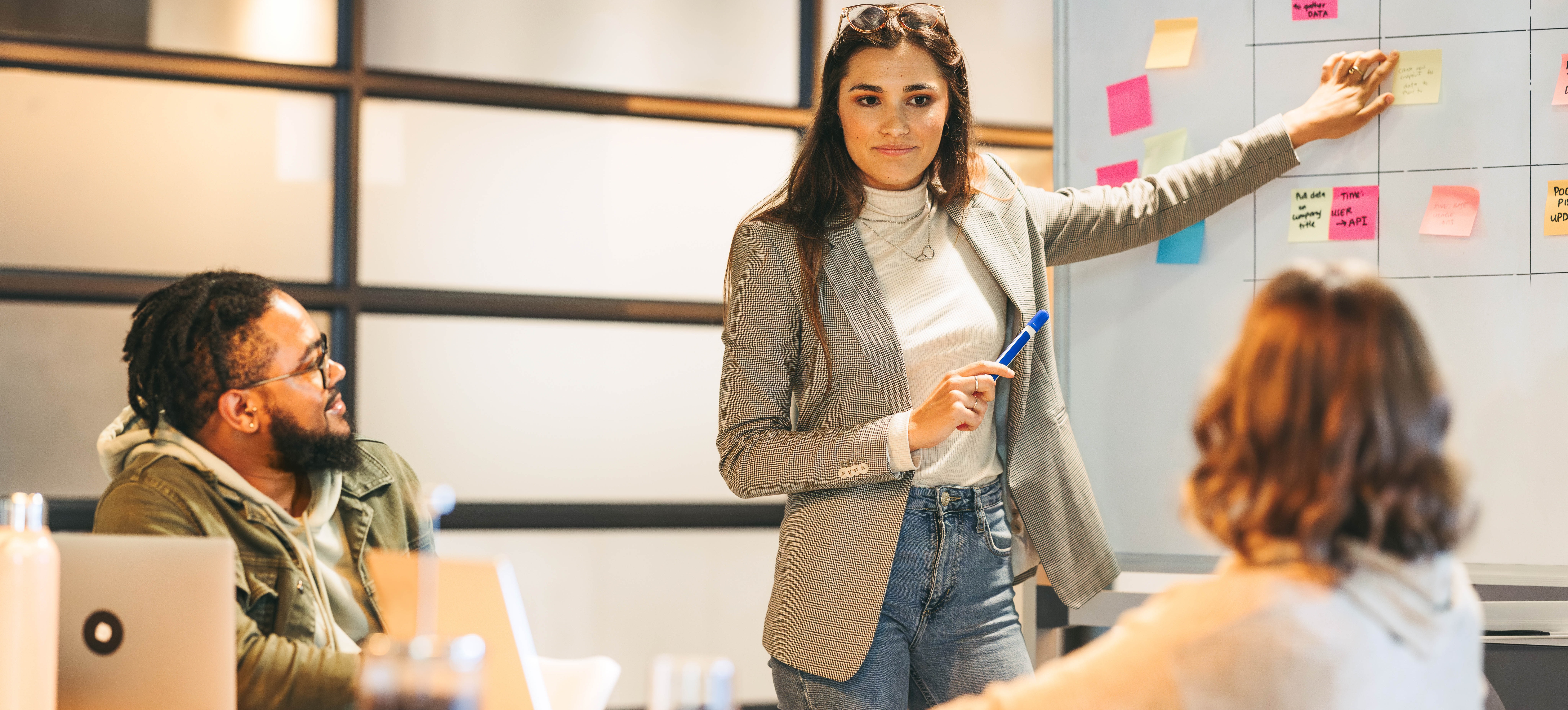 [Featured Image] A vice president of sales and marketing, which is one of the highest-paying business jobs, points to notes on a whiteboard as she talks with her team in an office setting.