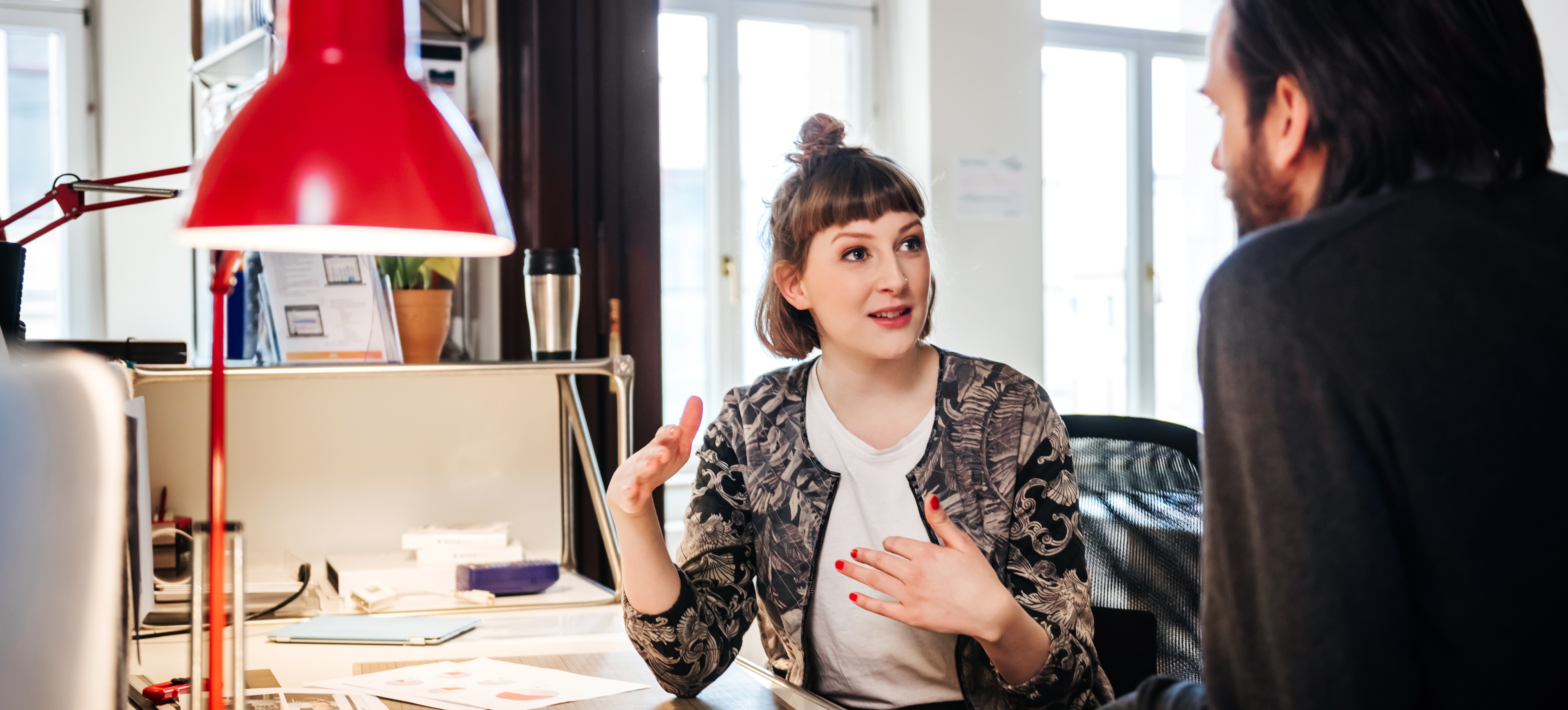 [Feature Image] An aspiring designer meets with their mentor for advice on the best graphic design portfolio examples to include in their portfolio.
