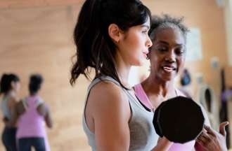 [Featured image] A fitness trainer in a pink shirt instructs a client on how to properly perform an exercise with dumbbells.