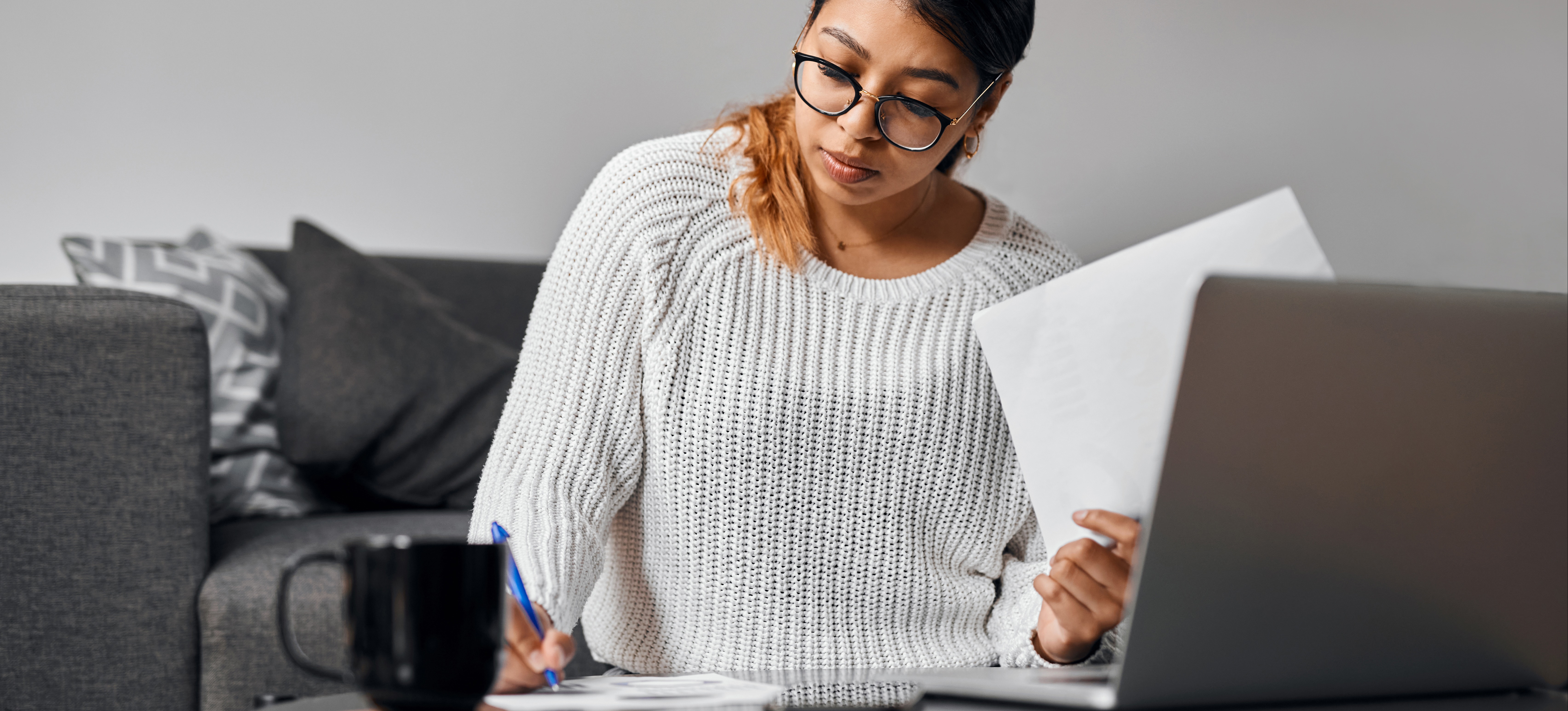 [Featured Image: A young student takes notes as they sit in front of a computer and study for an online MBA]