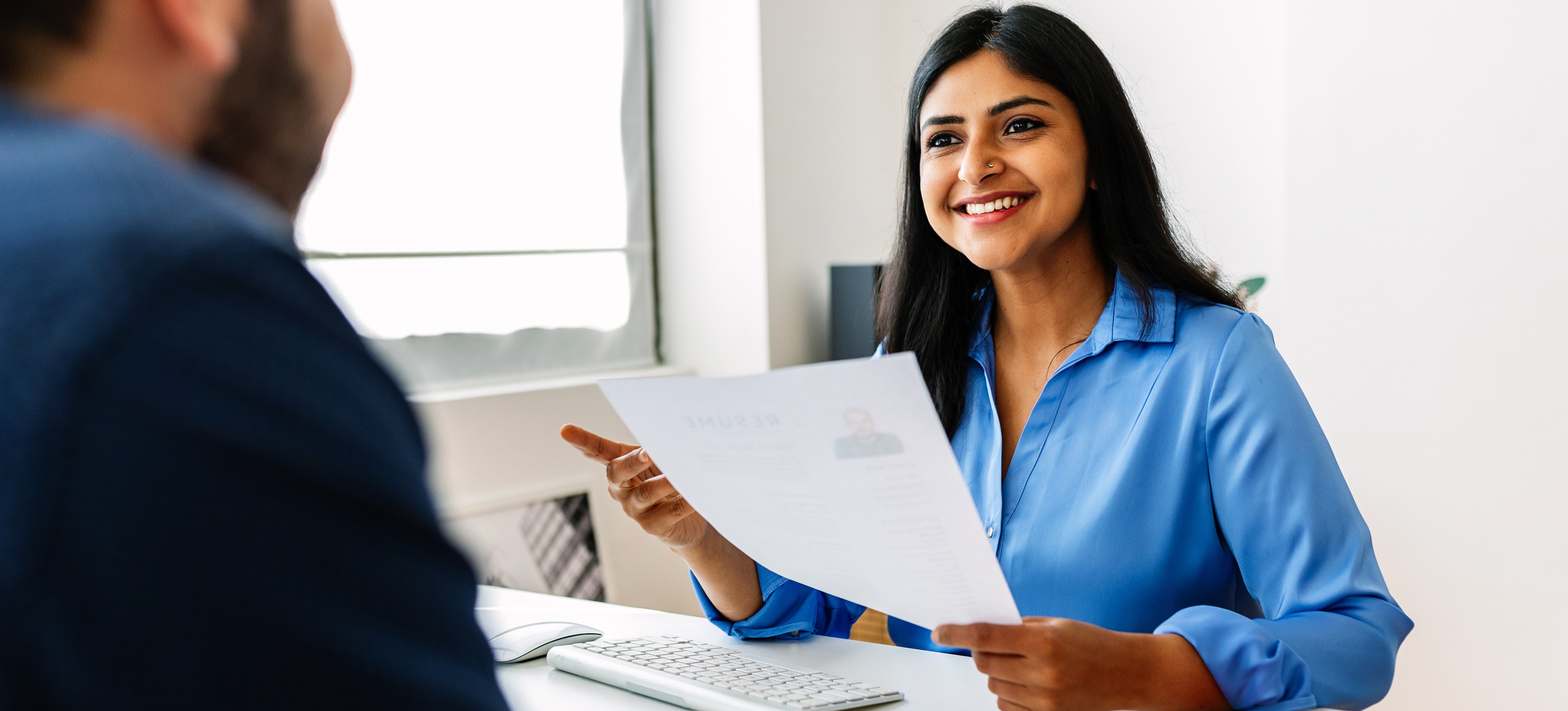 [Featured Image]: A woman in an office smiles after successfully answering teacher interview questions.
