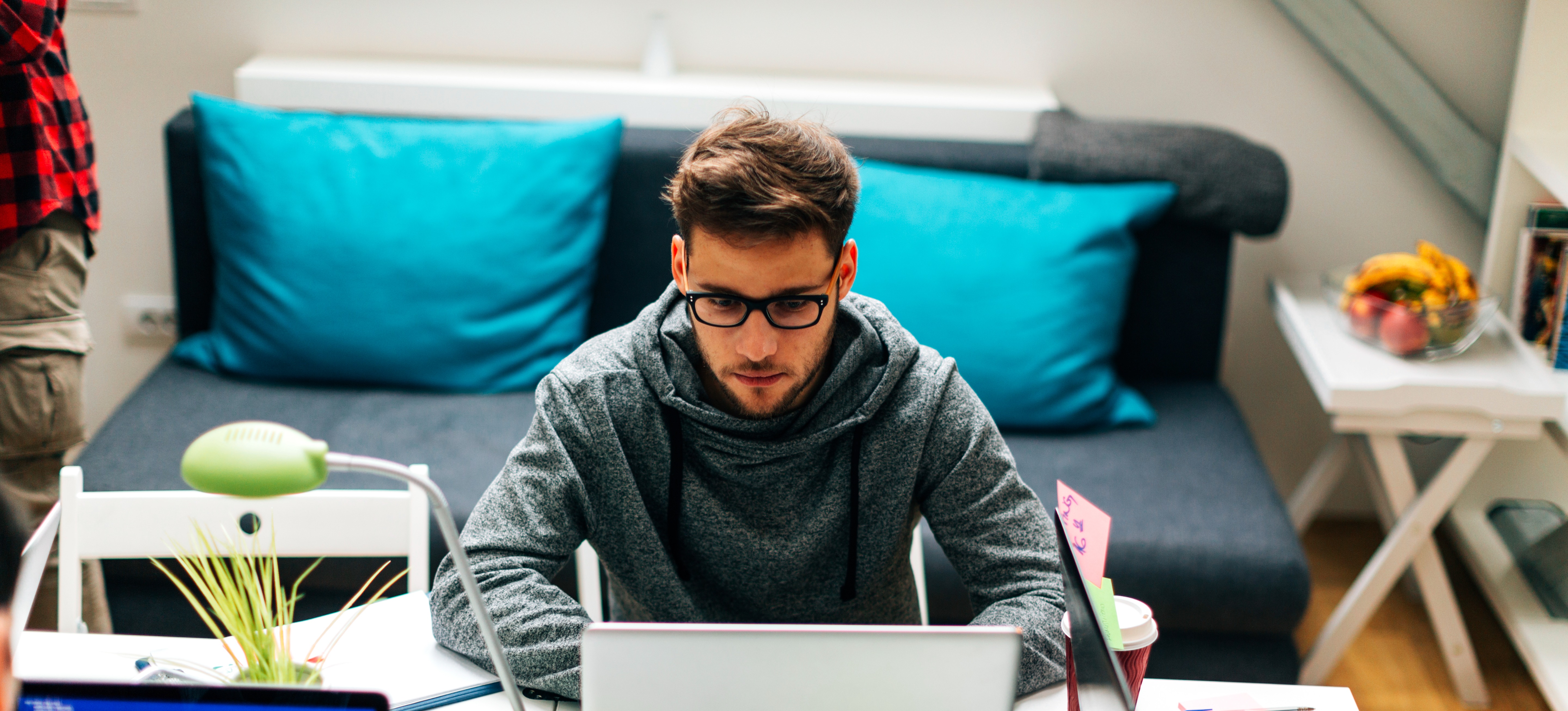 [Featured Image] A back-end developer in a gray sweatshirt uses their laptop to work on an API with nearby coworkers.

