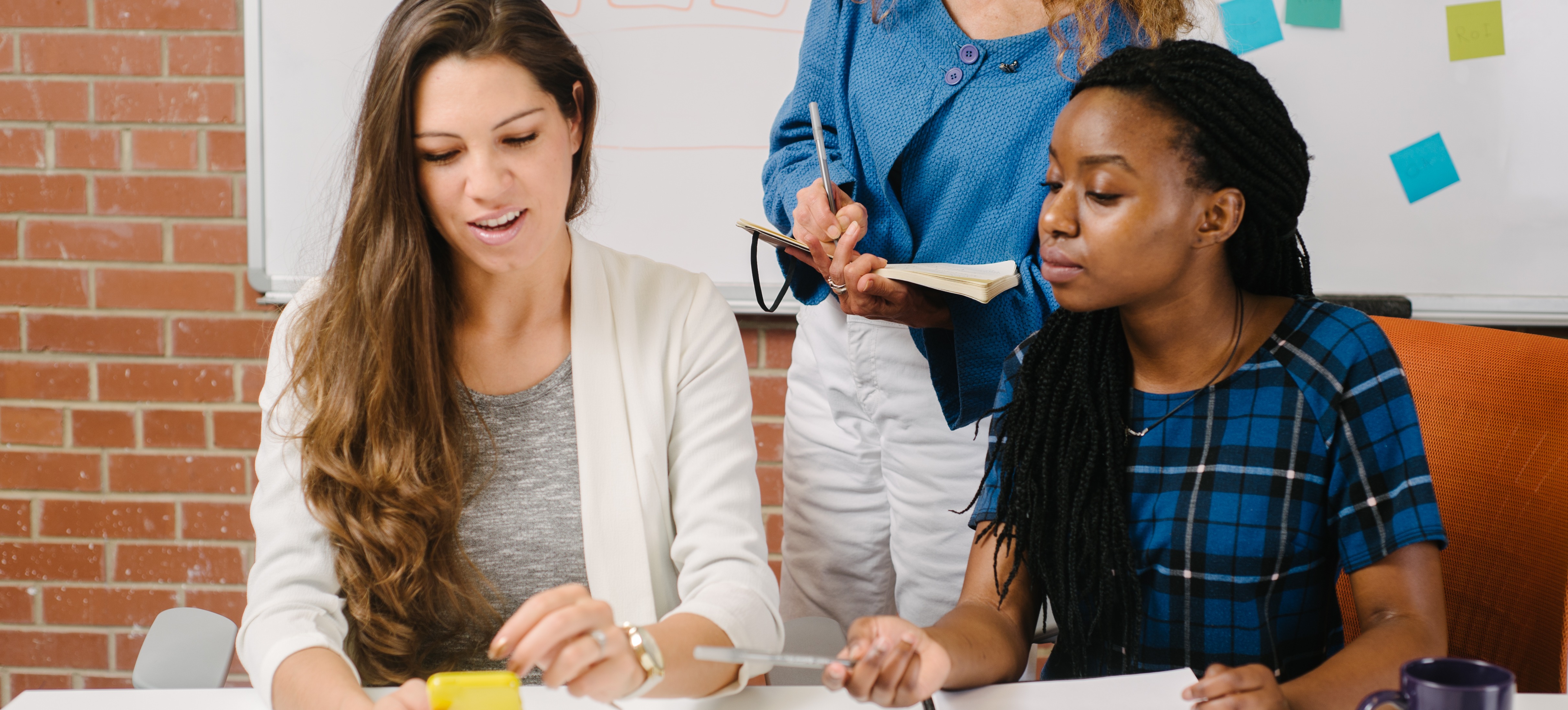 [Featured Image] Three mobile-friendly website developers gather around a mobile device to analyze a new application created using bootstrap.