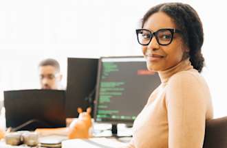 [Featured Image] A woman wearing glasses sits at a computer in an office.